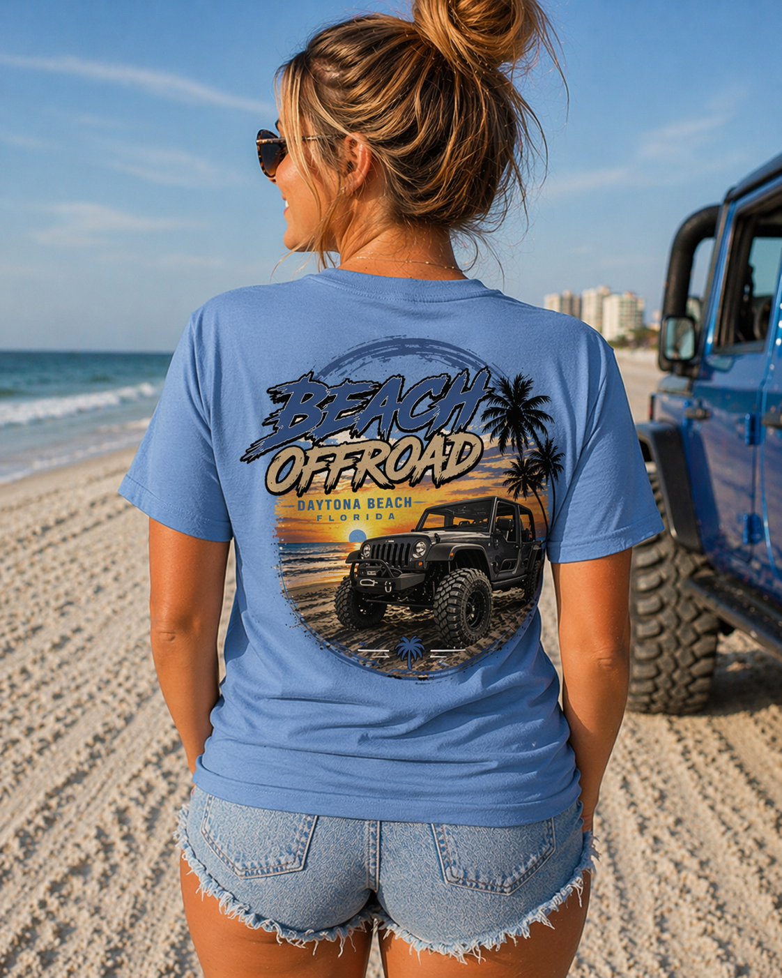 Woman wearing a blue Daytona Beach 'Beach Offroad' t-shirt on a beach with a jeep in the background.